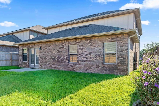 back of property with a yard, roof with shingles, fence, and brick siding