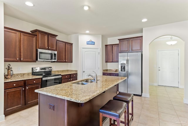 kitchen featuring arched walkways, a breakfast bar, a kitchen island with sink, stainless steel appliances, and a sink