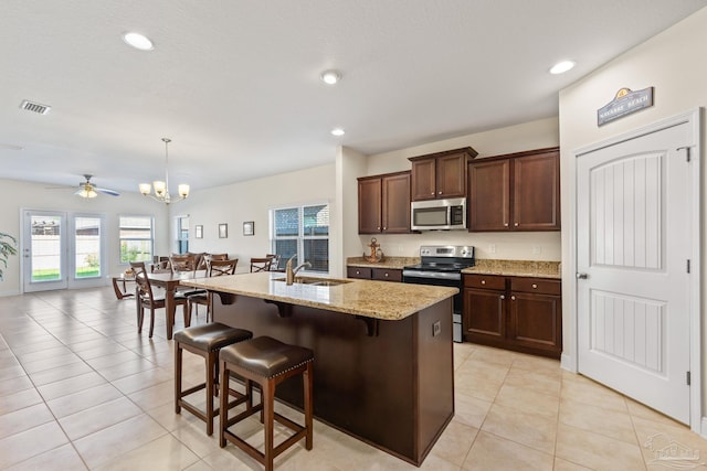 kitchen featuring light stone counters, a kitchen island with sink, stainless steel appliances, a breakfast bar, and a sink