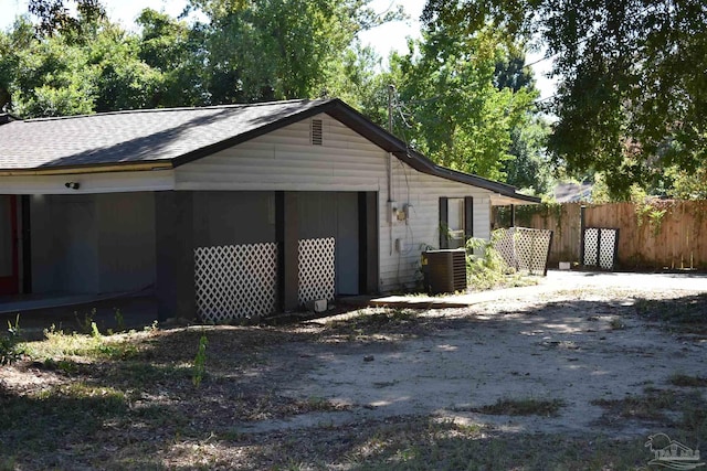 view of side of home with fence, roof with shingles, and central air condition unit