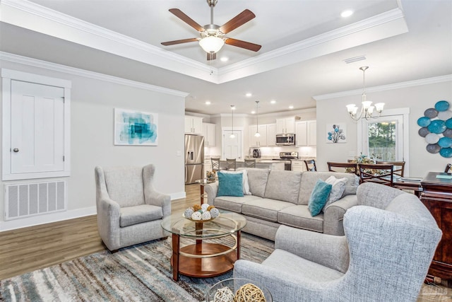 living room featuring a tray ceiling, ceiling fan with notable chandelier, wood-type flooring, and ornamental molding