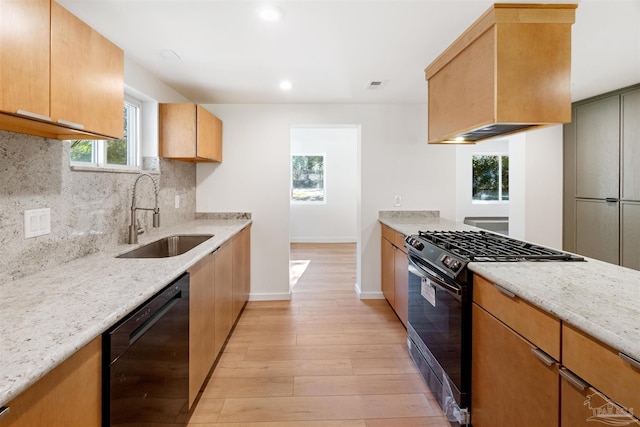 kitchen featuring sink, custom exhaust hood, light hardwood / wood-style flooring, light stone countertops, and black appliances