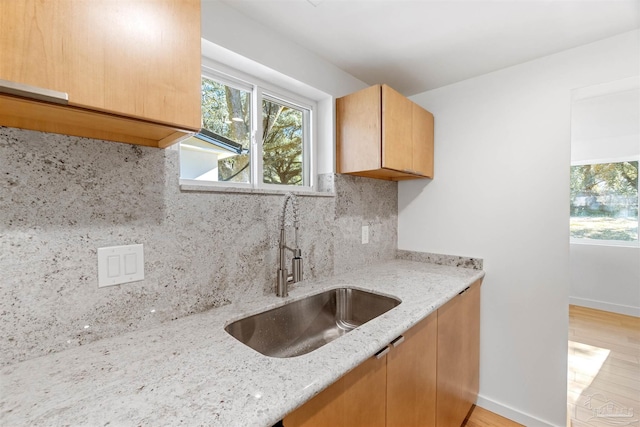 kitchen with light hardwood / wood-style floors, sink, light stone counters, and decorative backsplash