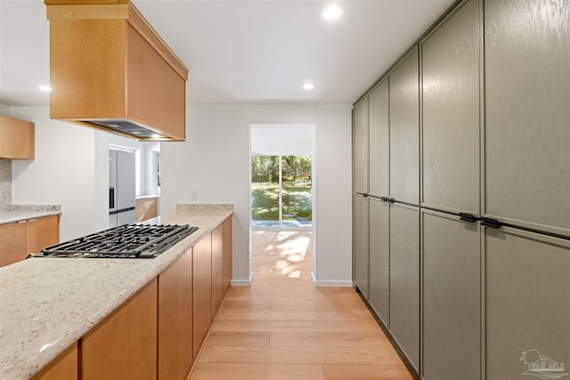 kitchen with gray cabinets, premium range hood, stainless steel gas cooktop, light stone countertops, and light wood-type flooring