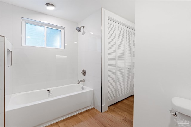 bathroom with wood-type flooring, toilet, and tiled shower / bath combo