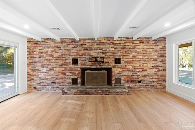 unfurnished living room featuring brick wall, beam ceiling, a brick fireplace, and light hardwood / wood-style flooring