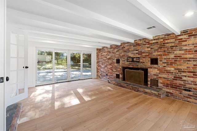 unfurnished living room with a fireplace, brick wall, beam ceiling, and light hardwood / wood-style floors