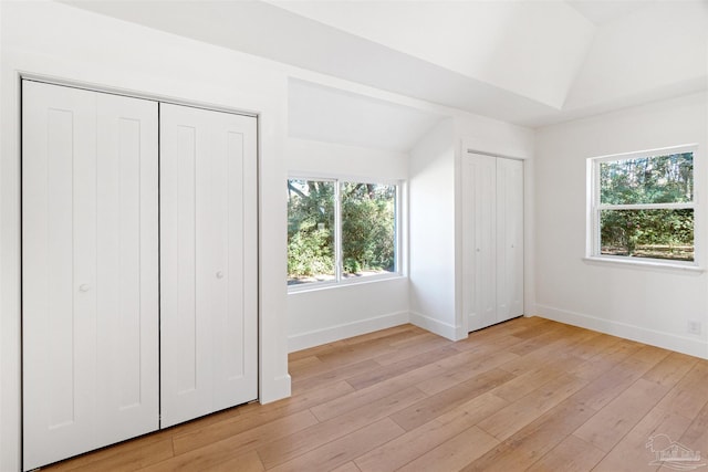 unfurnished bedroom with lofted ceiling, two closets, and light hardwood / wood-style flooring