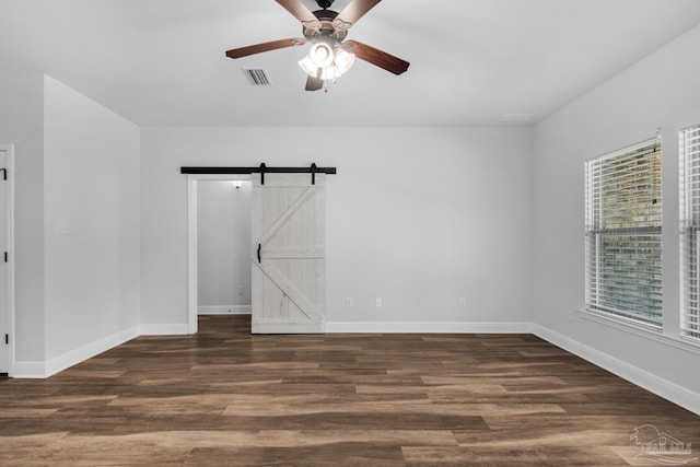 empty room with baseboards, wood finished floors, ceiling fan, and a barn door