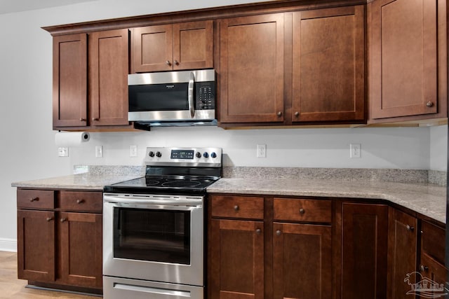 kitchen with light wood finished floors, light stone countertops, and appliances with stainless steel finishes