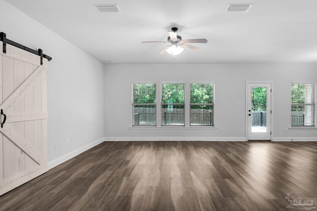 unfurnished living room featuring dark wood-style flooring, visible vents, ceiling fan, and a barn door