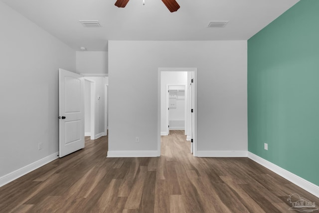 unfurnished bedroom with a walk in closet, dark wood finished floors, visible vents, and baseboards