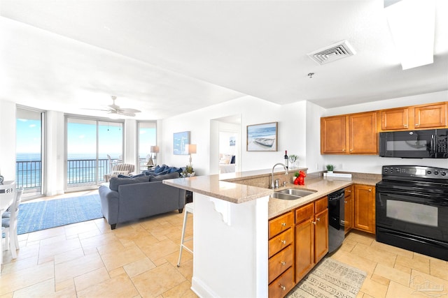 kitchen with black appliances, kitchen peninsula, sink, a kitchen bar, and a wall of windows