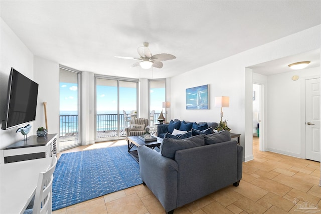 living room with ceiling fan, a water view, and a wall of windows