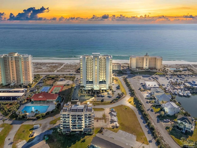 aerial view at dusk featuring a water view and a view of the beach