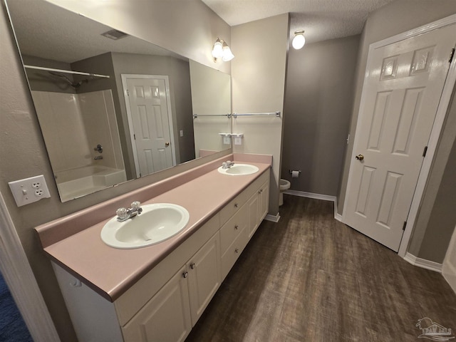 bathroom with a sink, double vanity, toilet, and wood finished floors