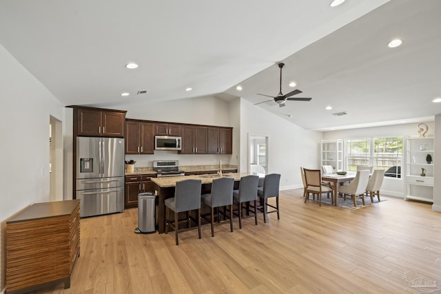 kitchen featuring stainless steel appliances, a sink, a breakfast bar, lofted ceiling, and a kitchen island with sink