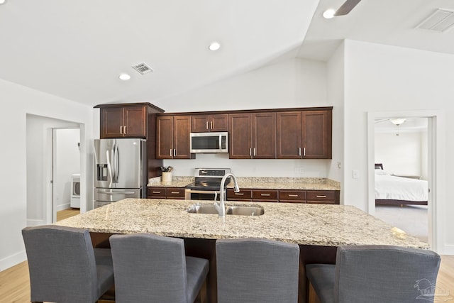 kitchen with stainless steel appliances, a sink, a breakfast bar, vaulted ceiling, and light wood finished floors