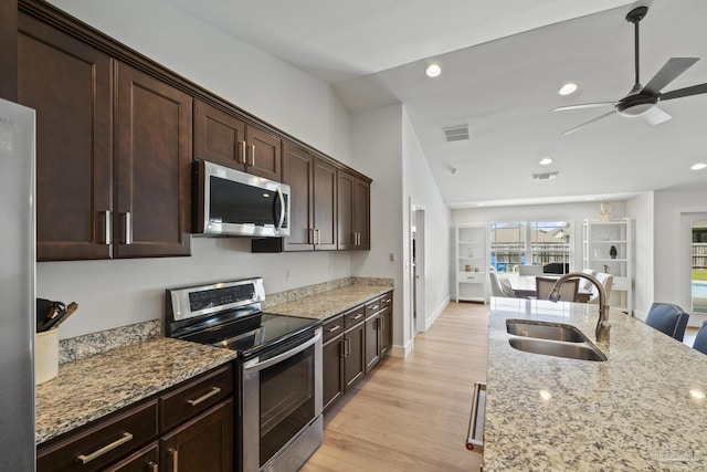kitchen featuring appliances with stainless steel finishes, a sink, light stone countertops, ceiling fan, and light wood-style floors