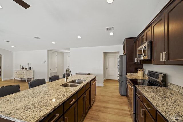 kitchen featuring stainless steel appliances, a sink, a kitchen island with sink, baseboards, and light wood-type flooring