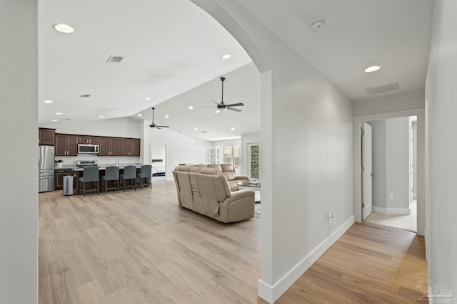 living room with arched walkways, lofted ceiling, light wood-style flooring, ceiling fan, and recessed lighting