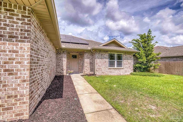 entrance to property featuring brick siding, a shingled roof, and solar panels