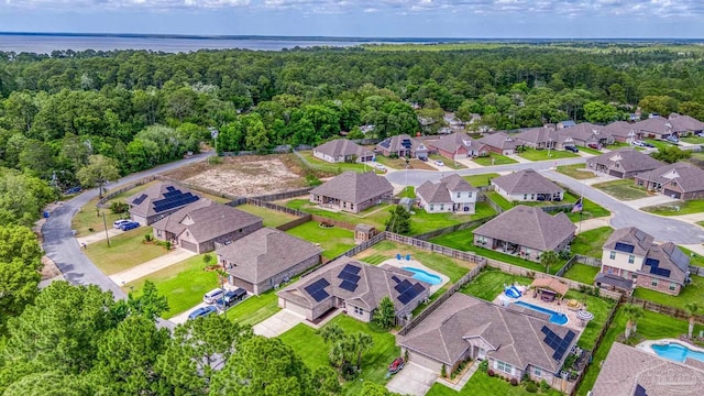 aerial perspective of suburban area featuring a pool, a heavily wooded area, and a large body of water