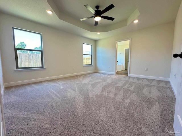 spare room with ceiling fan, light carpet, and a tray ceiling