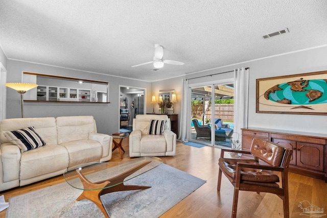 living area featuring ornamental molding, a textured ceiling, visible vents, ceiling fan, and wood finished floors