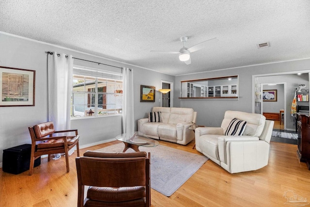 living room with light wood-type flooring, a ceiling fan, visible vents, and a textured ceiling
