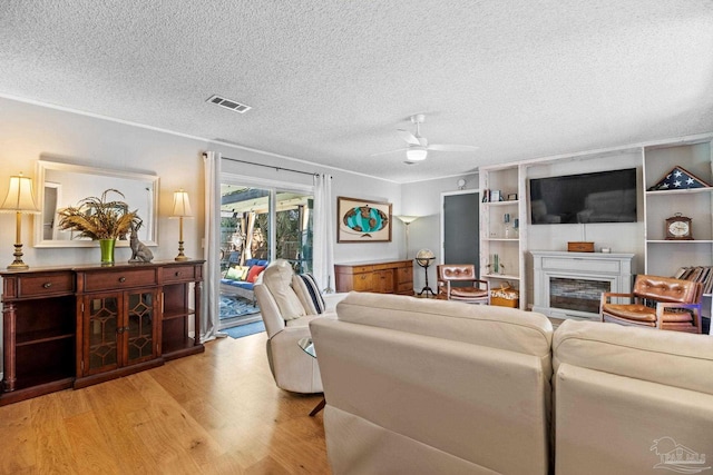 living room featuring visible vents, a ceiling fan, light wood-style floors, a fireplace, and a textured ceiling