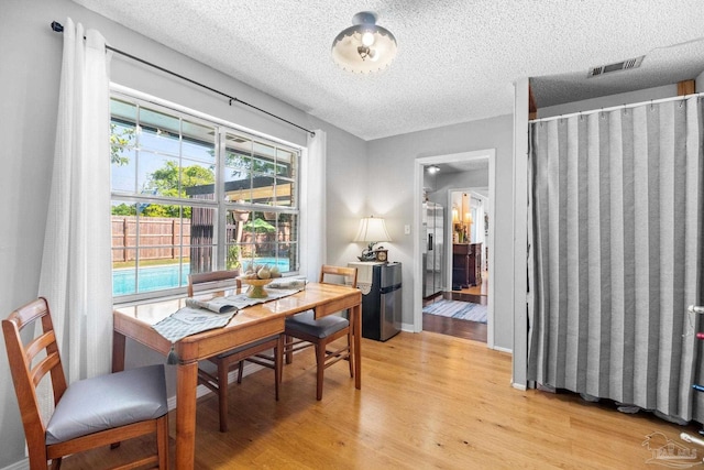 dining room with light wood finished floors, visible vents, a textured ceiling, and baseboards