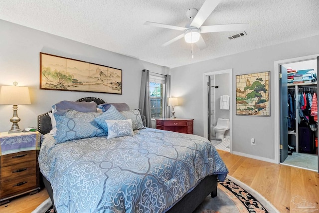 bedroom featuring a spacious closet, visible vents, a textured ceiling, and wood finished floors