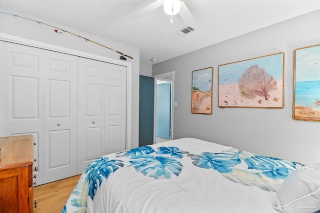 bedroom featuring visible vents, a closet, a ceiling fan, light wood-style floors, and a textured ceiling
