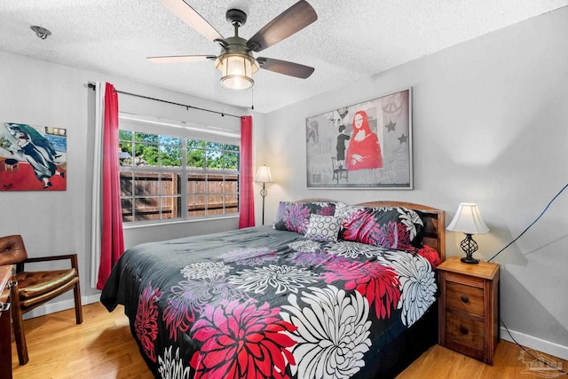 bedroom with ceiling fan, baseboards, wood finished floors, and a textured ceiling