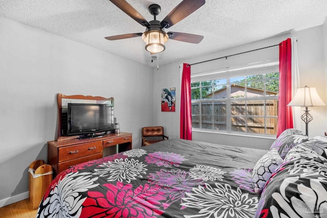 bedroom with ceiling fan, a textured ceiling, baseboards, and wood finished floors