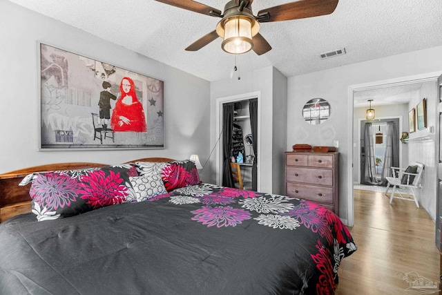 bedroom with visible vents, a ceiling fan, wood finished floors, and a textured ceiling