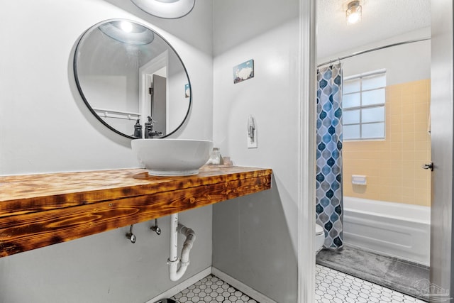 bathroom with shower / bathtub combination with curtain, toilet, a sink, tile patterned floors, and baseboards