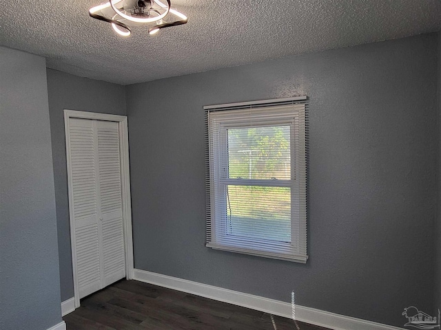 unfurnished bedroom featuring a textured ceiling, dark hardwood / wood-style flooring, and a closet