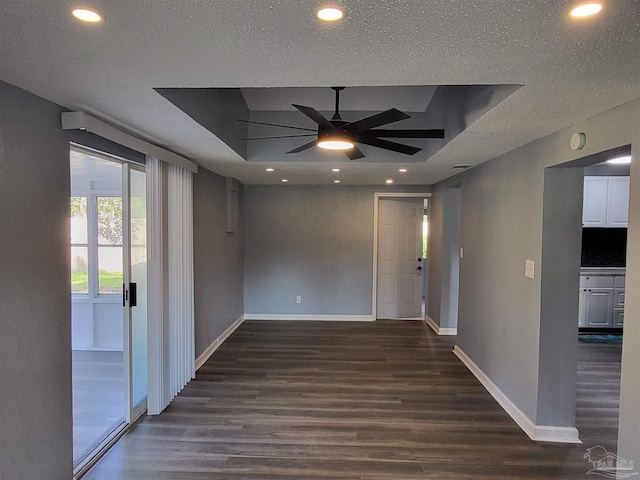 empty room with a tray ceiling, ceiling fan, dark wood-type flooring, and a textured ceiling