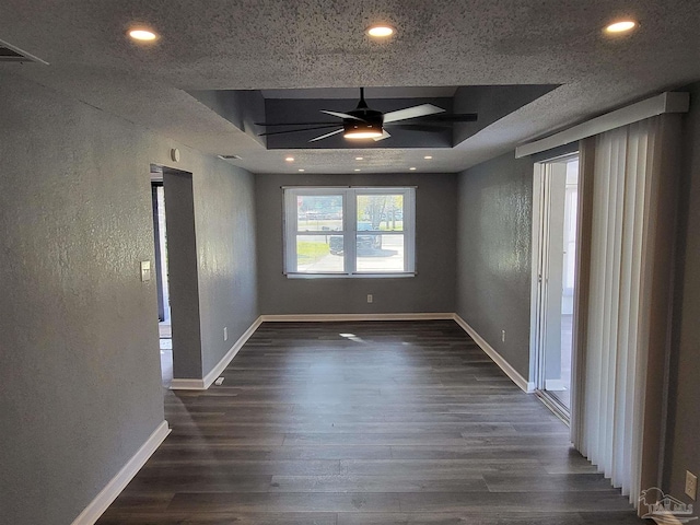 empty room with a textured ceiling, a raised ceiling, ceiling fan, and dark wood-type flooring