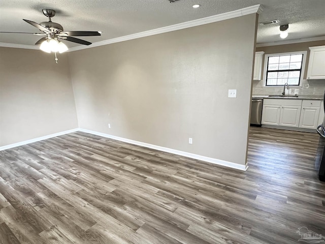 spare room with a sink, wood finished floors, baseboards, visible vents, and crown molding