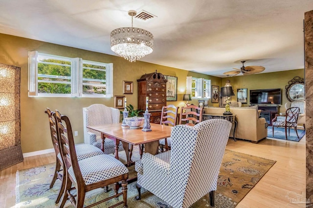 dining space with ceiling fan with notable chandelier and light hardwood / wood-style flooring