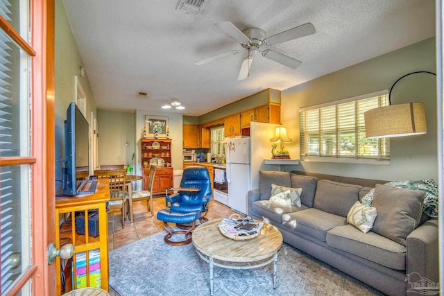 living room featuring ceiling fan, light tile patterned flooring, and a textured ceiling