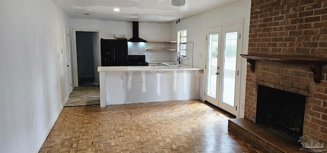 kitchen with tasteful backsplash, wall chimney exhaust hood, a sink, a fireplace, and black fridge