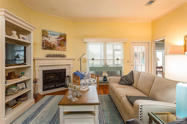 living room with a tiled fireplace, hardwood / wood-style floors, and crown molding