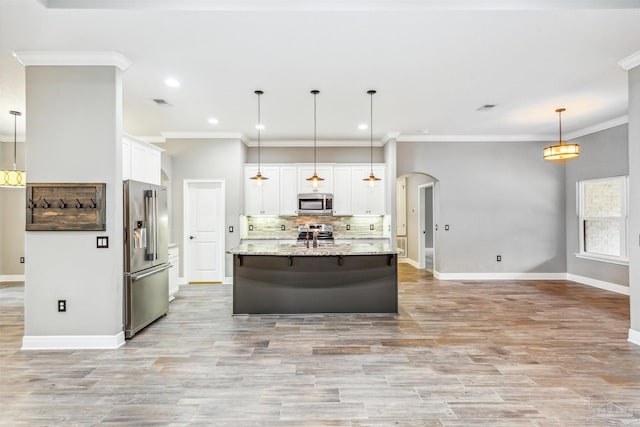 kitchen with pendant lighting, white cabinets, light stone countertops, an island with sink, and stainless steel appliances