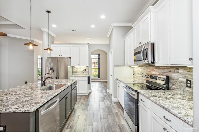 kitchen with white cabinets, appliances with stainless steel finishes, hanging light fixtures, and an island with sink