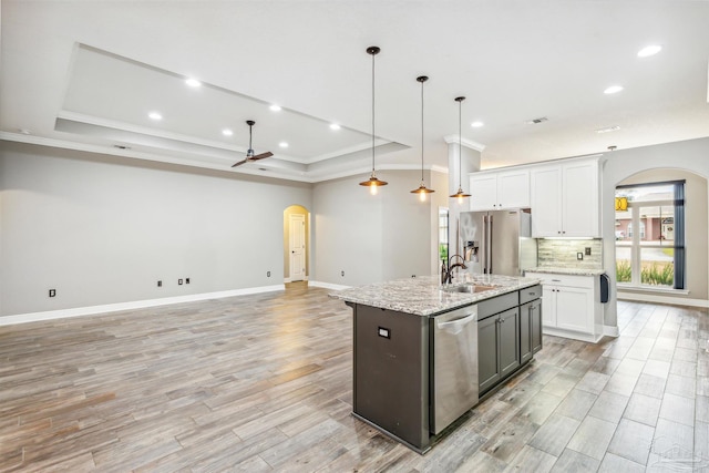 kitchen with white cabinetry, stainless steel appliances, pendant lighting, a center island with sink, and light wood-type flooring