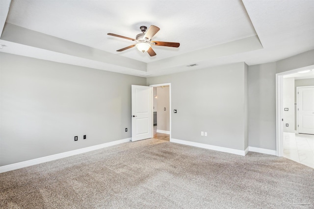 spare room with light carpet, a tray ceiling, and ceiling fan